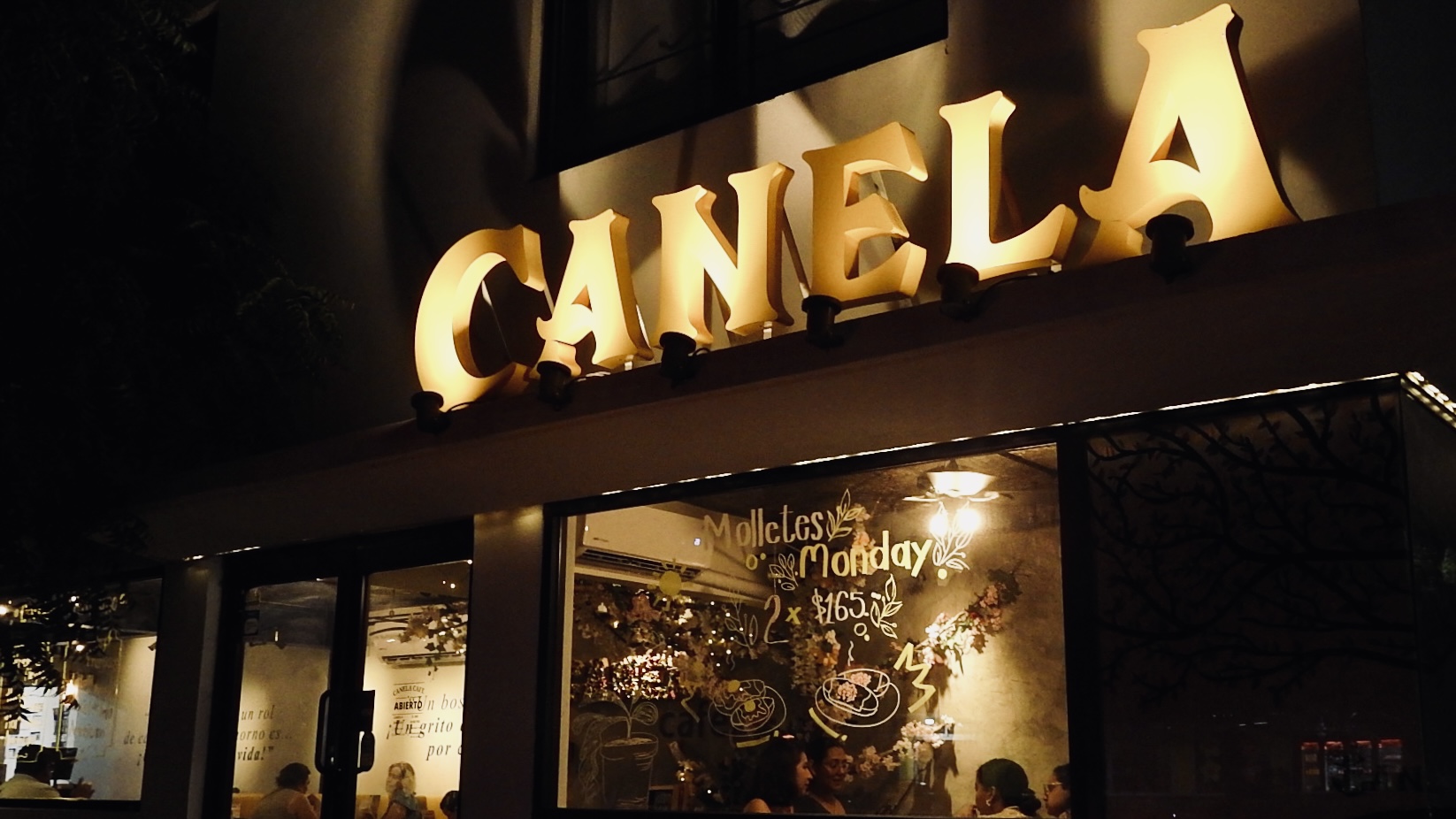 Fachada de Canela Café de noche con letrero iluminado